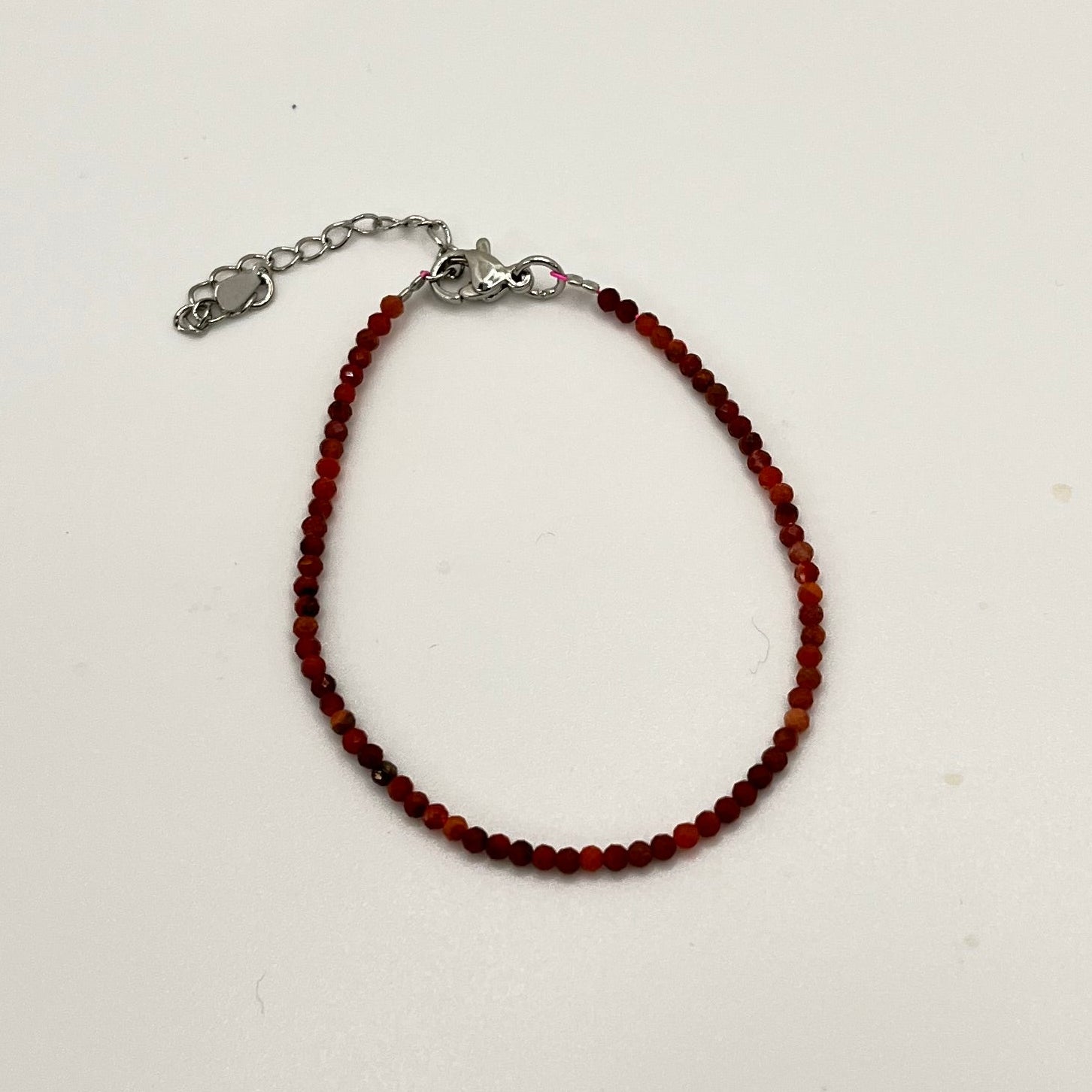 Bracelet of small faceted red and black marbled beads with a silver colored chain and findings. 