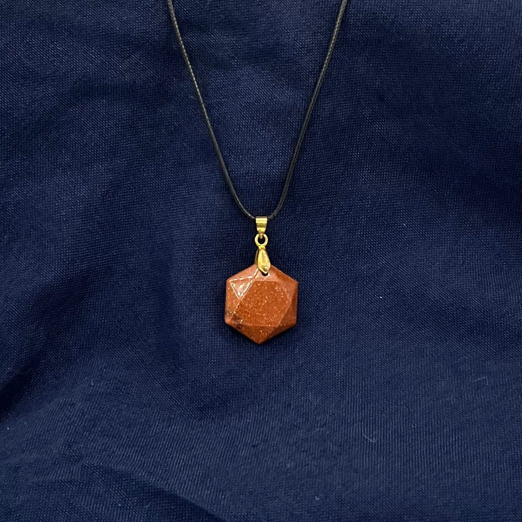 Orange sparkling semi-flat hexagon crystal hanging from a black cord on a blue fabric background.