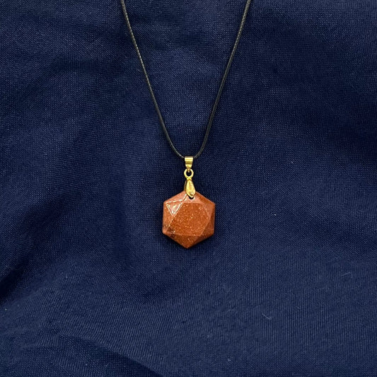 Orange sparkling semi-flat hexagon crystal hanging from a black cord on a blue fabric background.