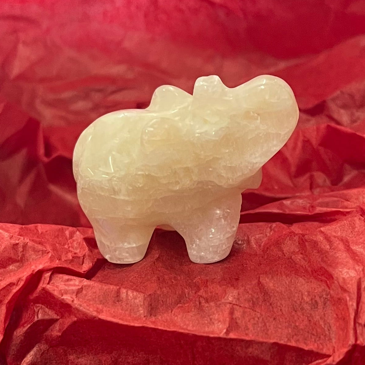 A small carved pale stone figurine of an elephant, resting on crumpled red tissue paper.