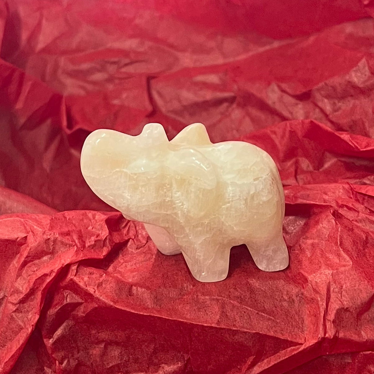 A small carved pale stone figurine of an elephant, resting on crumpled red tissue paper.