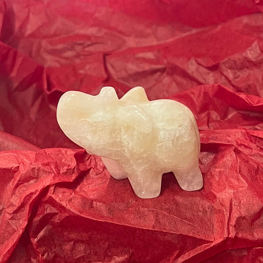 A small carved pale stone figurine of an elephant, resting on crumpled red tissue paper.