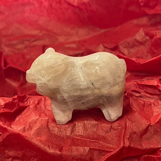 A small beige ceramic pig figurine, on red tissue paper