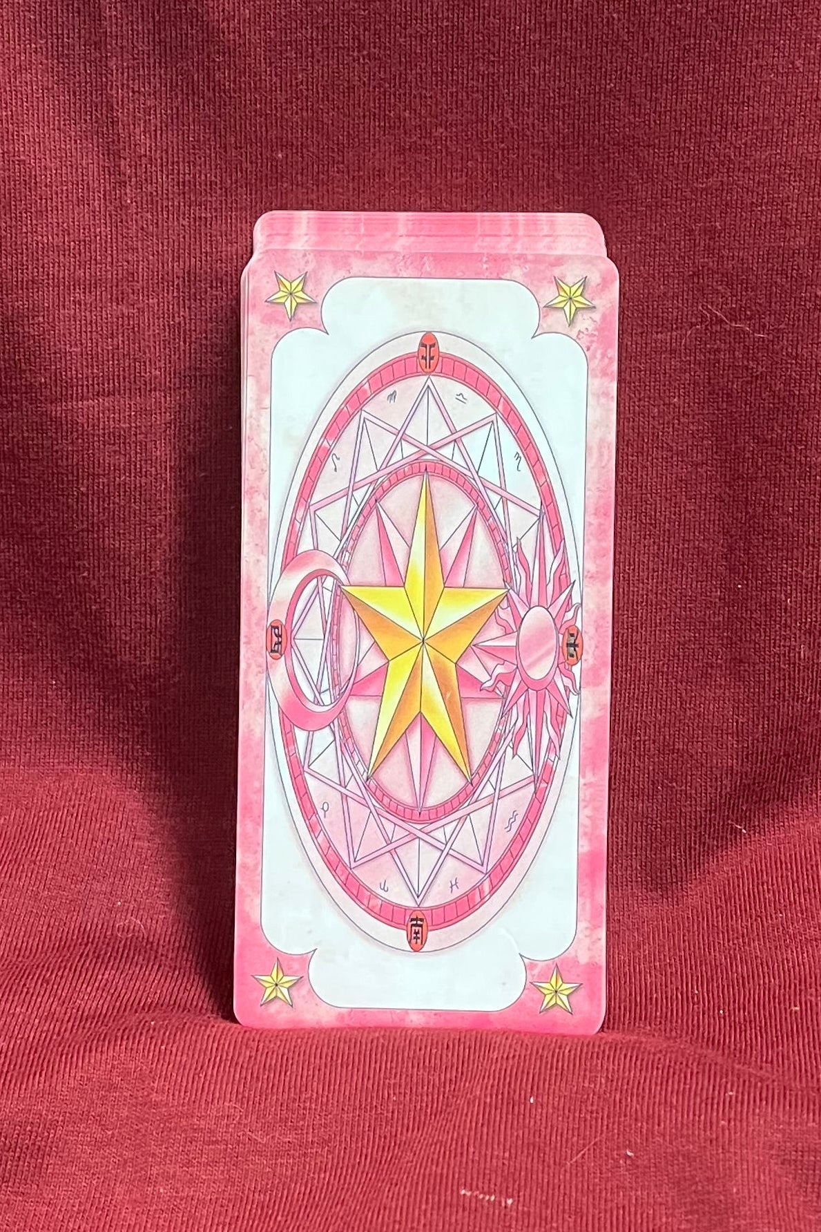A pink and white card standing upright on a red fabric surface, the back is a yellow star inside two Pink circles with webbing. 