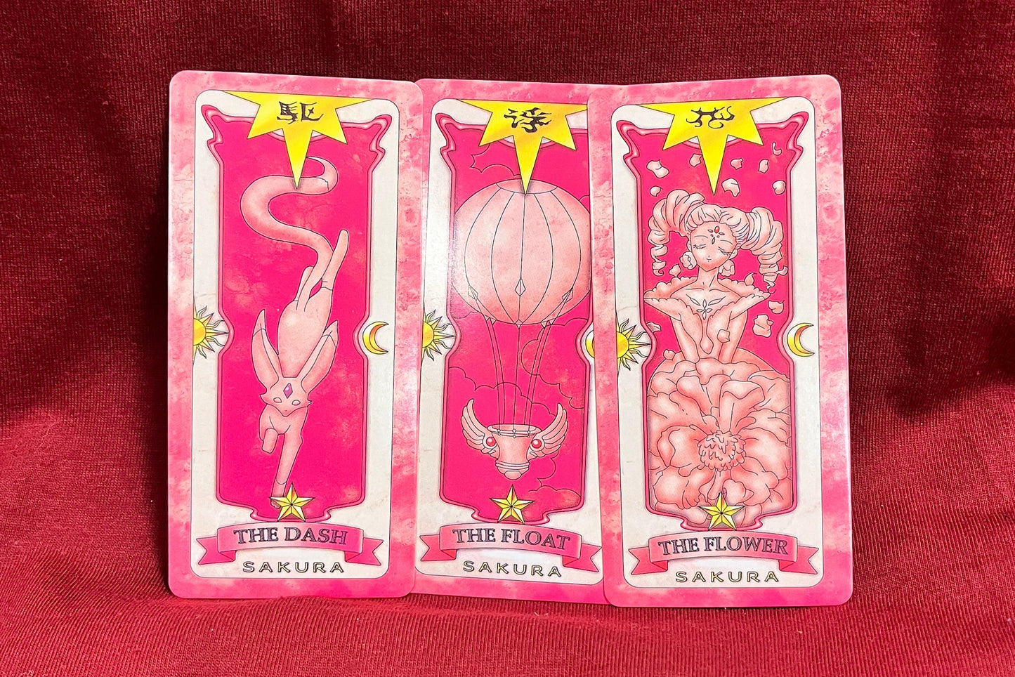 Three pink tarot cards fanned out on a red fabric background.