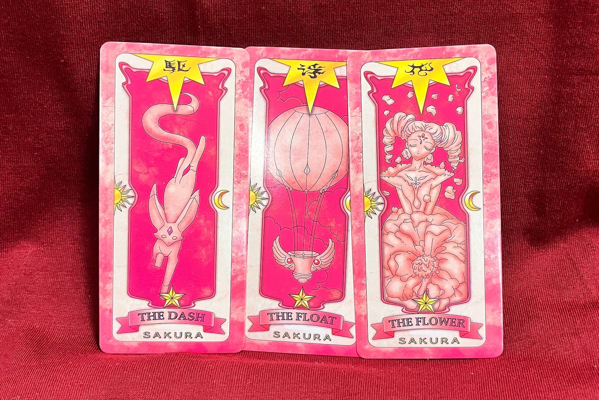 Three pink tarot cards fanned out on a red fabric background.