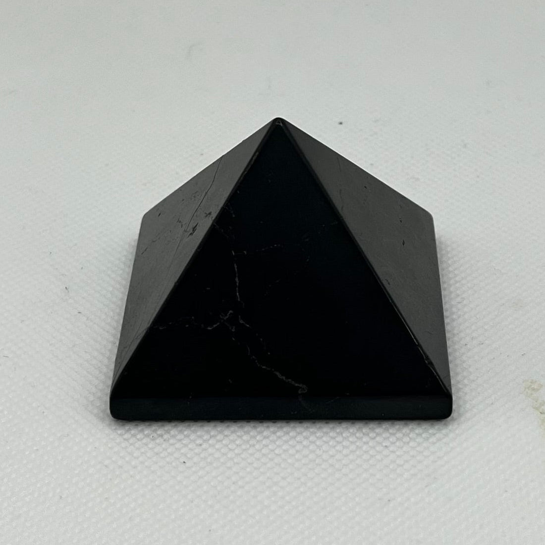 A small black pyramid crystal tower made of polished stone, standing upright on a white textured surface against a white background.