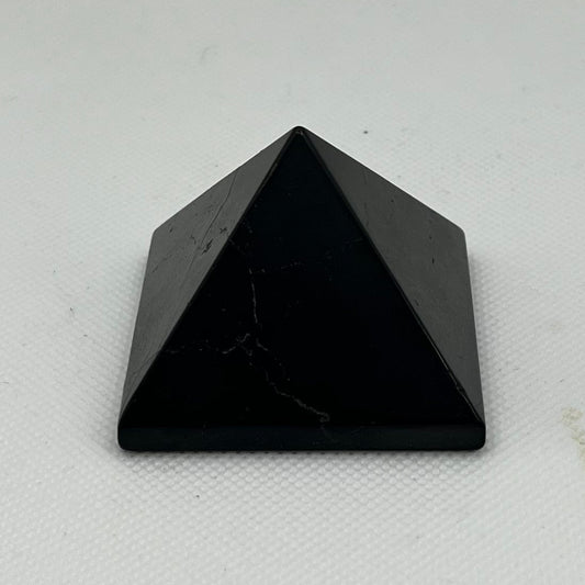 A small black pyramid crystal tower made of polished stone, standing upright on a white textured surface against a white background.