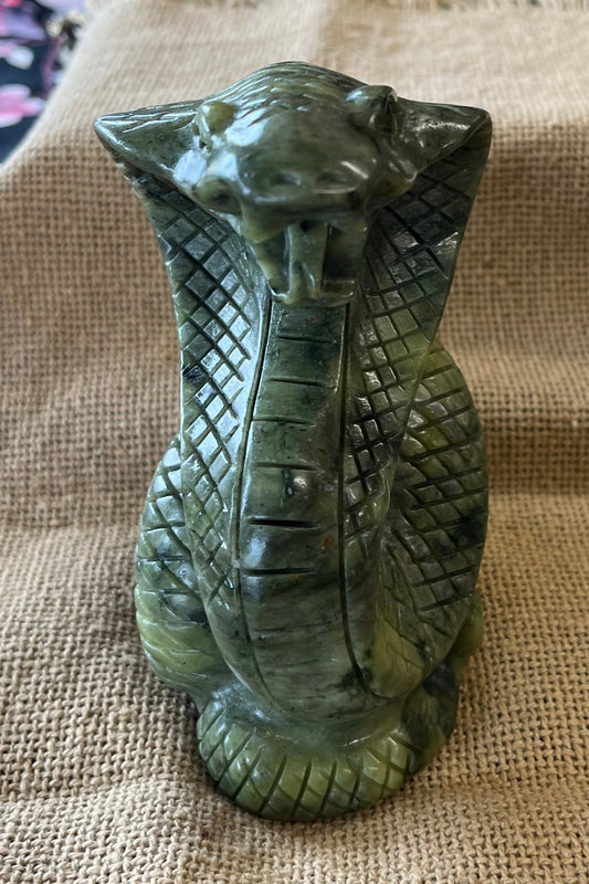 A green jade cobra statue on a tan background.  The cobra is standing up and its fangs are showing.