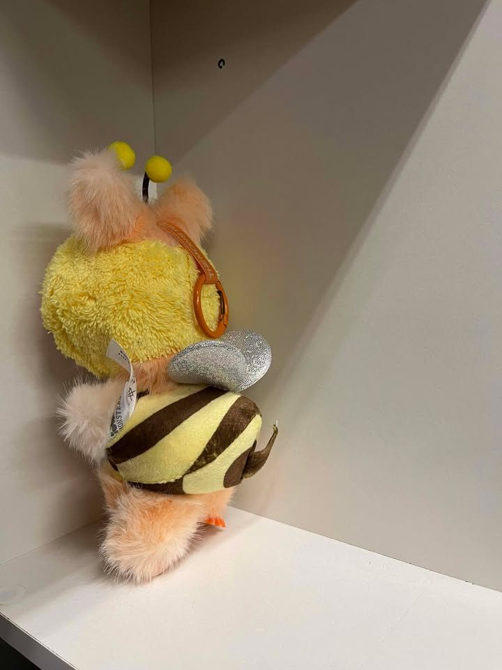 Plush toy resembling a bee with a yellow body and black stripes on a white surface.