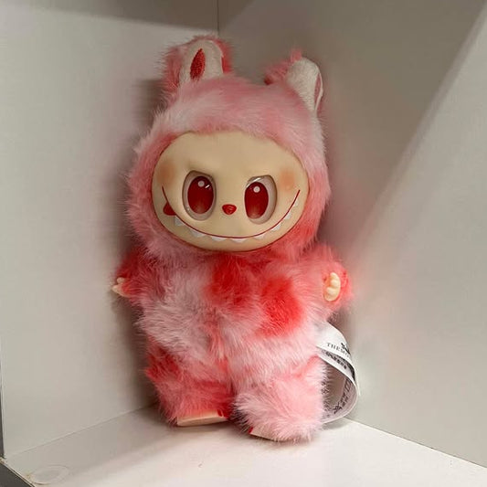 Plush toy with a fuzzy light and dark pink design on a white shelf.  It has red eyes, a red nose, a wide smile showing many teeth, a spot of blush on each cheek, and plastic hands and feet.  The feet have three toes with painted nails. 