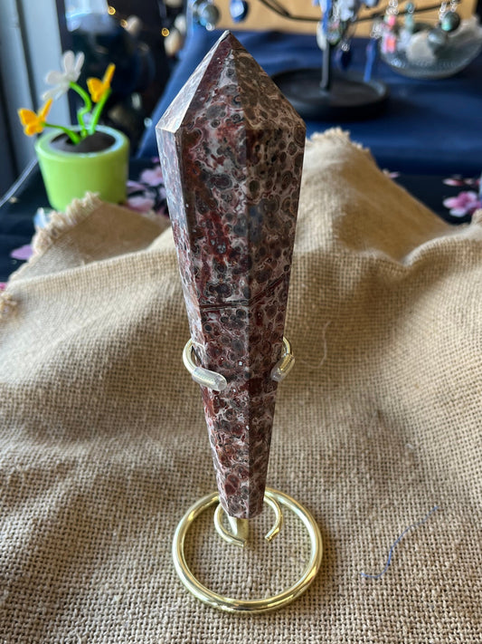 Brown, rust, and tan mottled crystal wand in a gold stand on a textured surface with a blurred background