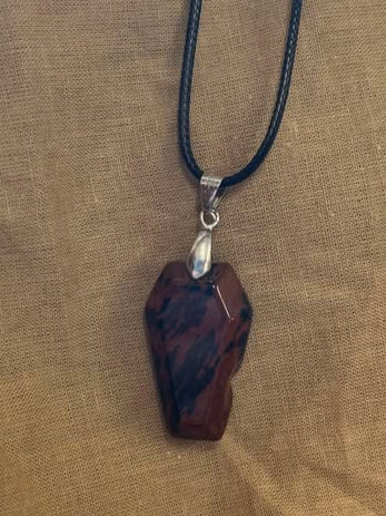 Red and black crystal coffin necklace with silver findings on a black cord, on a beige fabric background