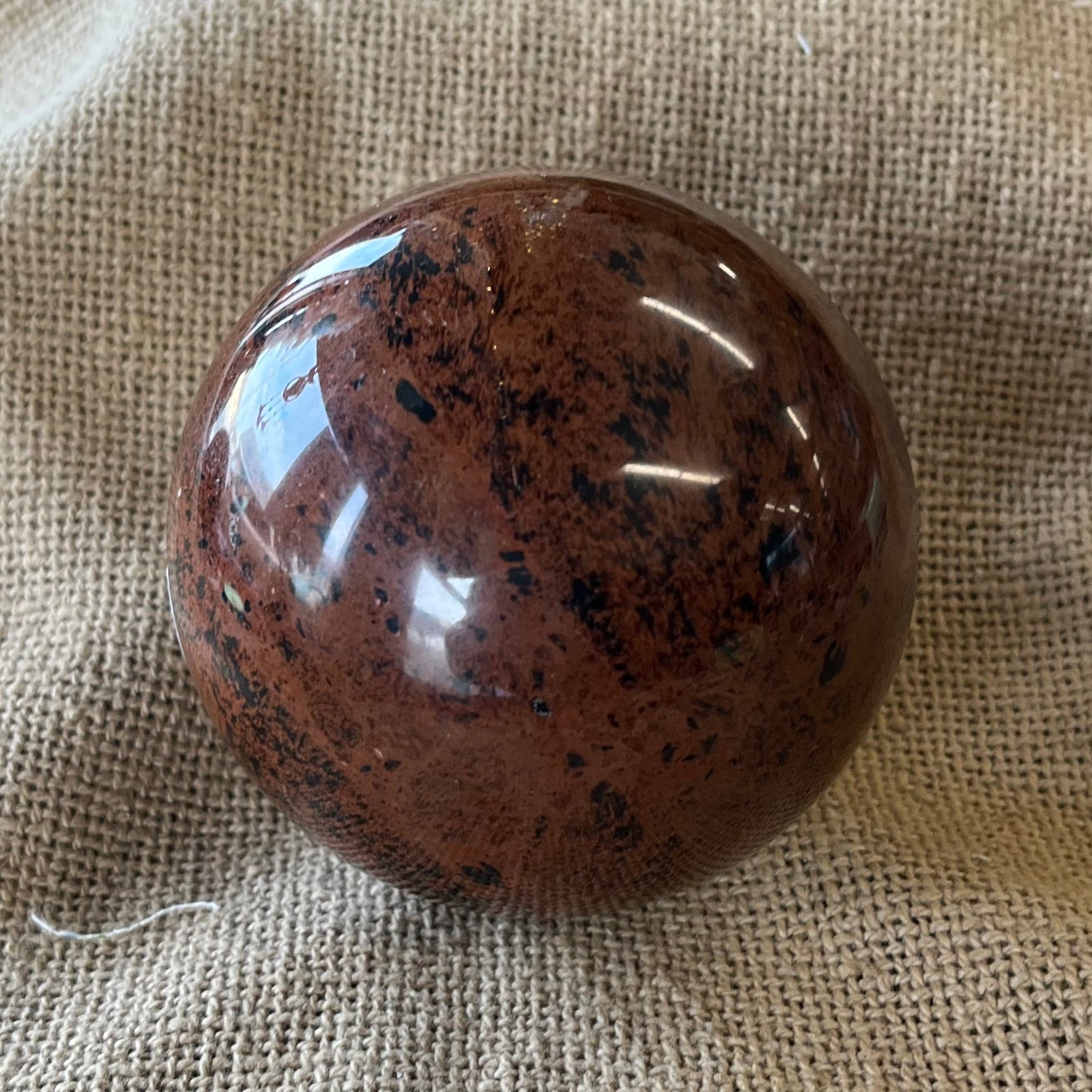 Red polished stone with black mottled inclusions on a textured beige fabric 