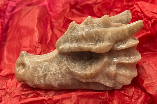 A carved dragon head from moonstone, a beige slightly iridescent stone. This is the side view.