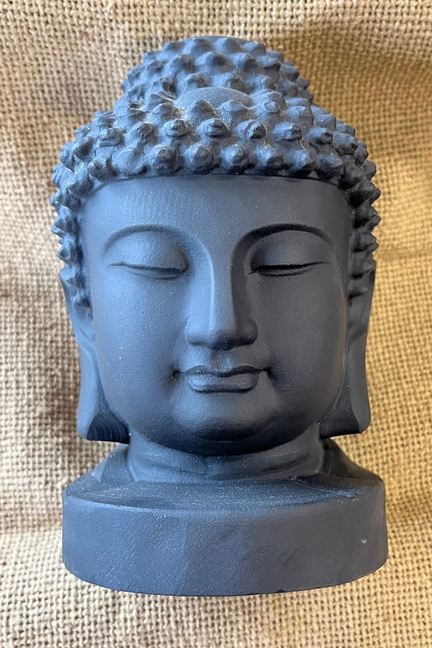 A charcoal gray buddha head sits on a textured tan background. 
