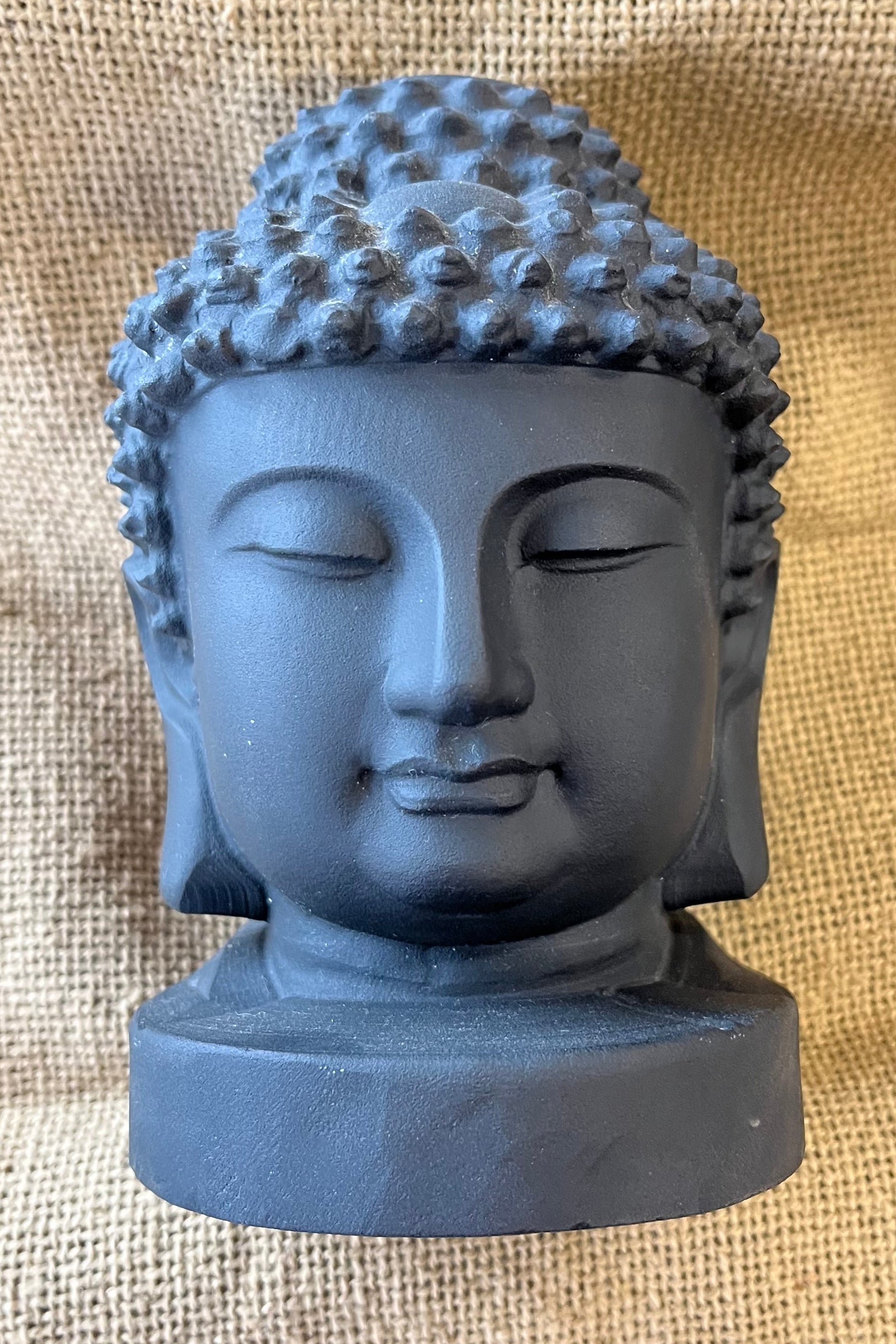 A charcoal gray buddha head sits on a textured tan background. 