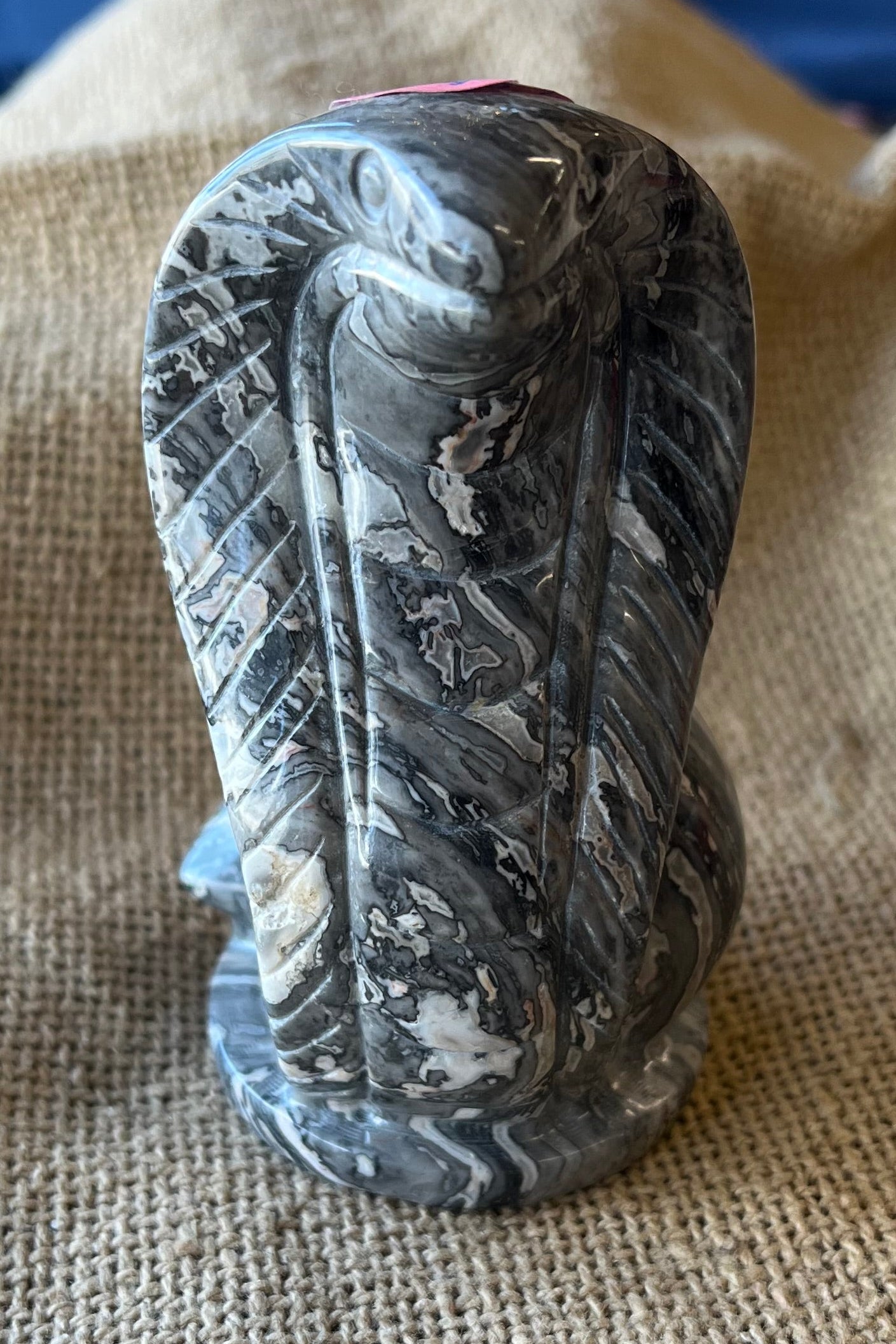 A marbled grey stone, in the shape of a cobra snake, stands on  flat base. 