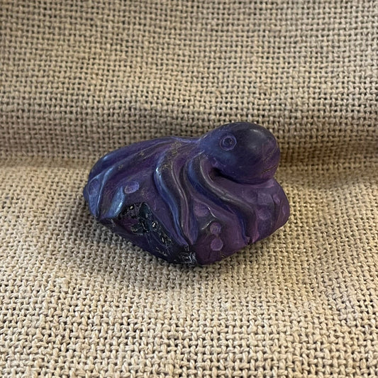 Purple sugilite carving of an octopus laying on a stone.