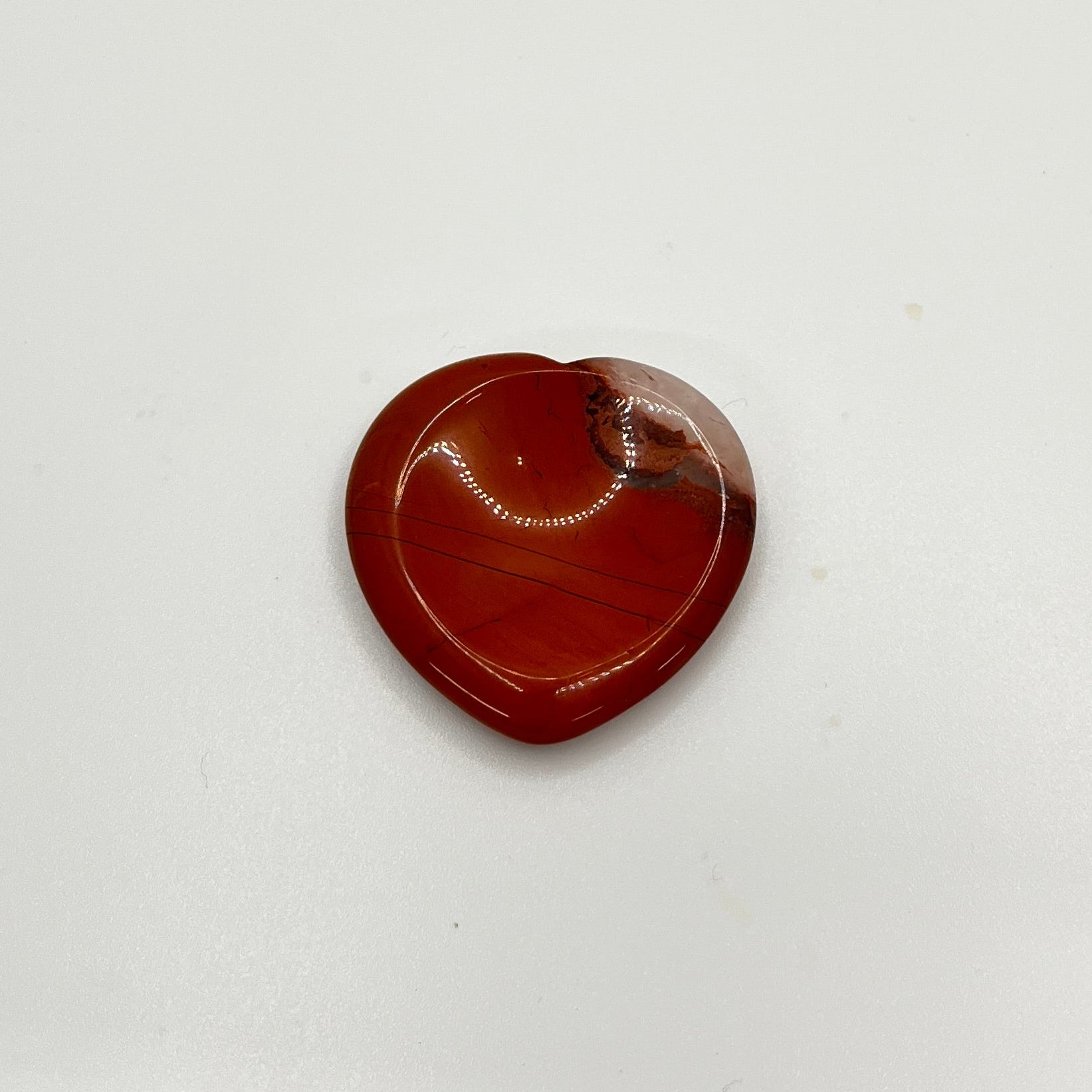 A red stone with white in the corner is in the shape of a heart, with a circular indented area in the middle to rub a thumb on.