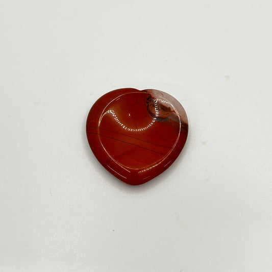 A red stone with white in the corner is in the shape of a heart, with a circular indented area in the middle to rub a thumb on.
