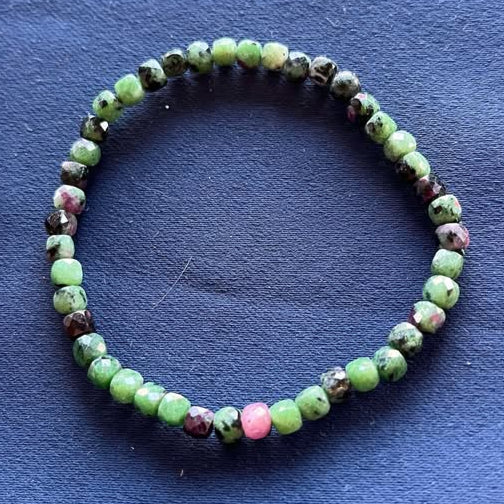 Beaded bracelet with green faceted beads with purple-ish pink and black spots on a blue background
