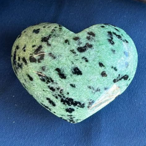 Heart-shaped mint green stone with black spots on a blue surface
