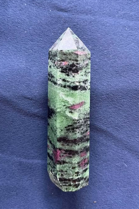 Green crystal tower with six sides and a point on the top, with purple and black marbled through the stone.
