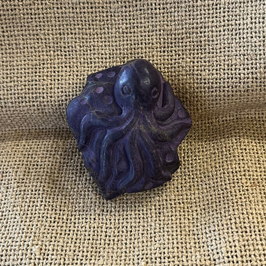 Purple sugilite carving of an octopus laying on a stone.