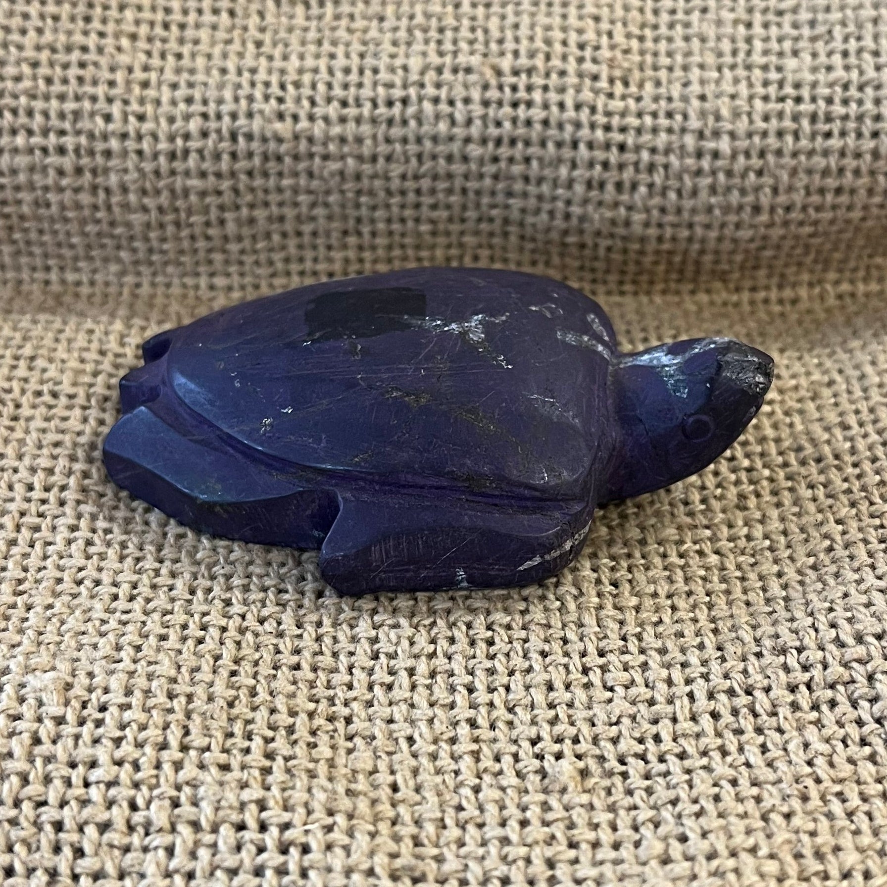 Decorative dark purple and white sea turtle figurine on a textured fabric surface