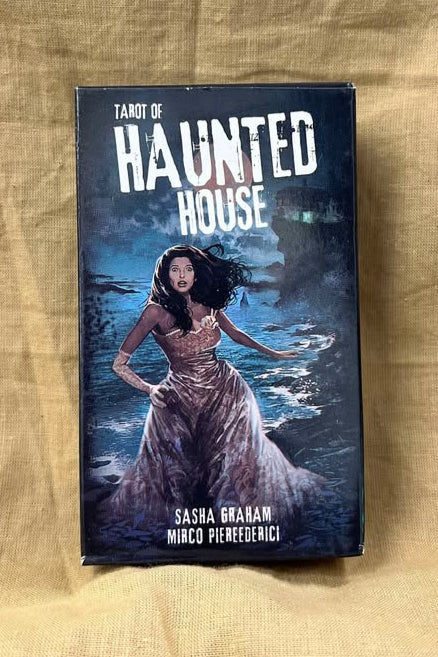 Tarot of Haunted House is printed at the top of a night scene in which a woman with dark hair wearing a pale dress runs along a shoreline with a home on a cliff in the background.