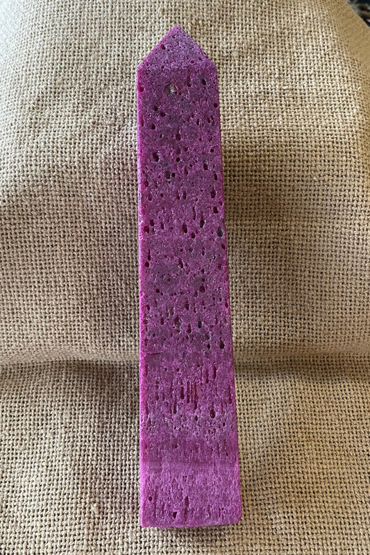 Purple-ish pink unpolished stone tower on a burlap background.