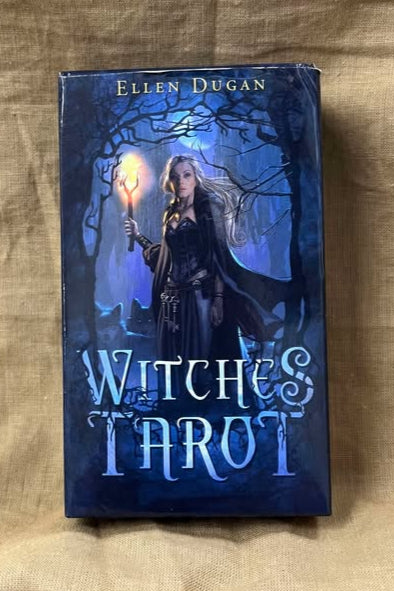 Tarot deck titled 'Witches Tarot' by Ellen Dugan features a blonde woman clad in a black dress, holding a torch as she walks through a woods at night.  