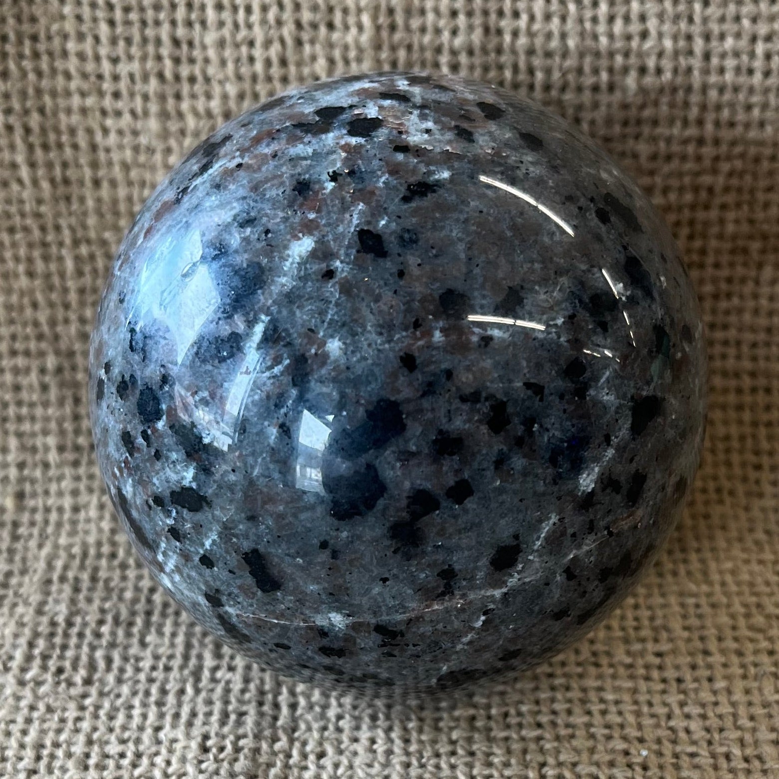 Gray black and tan crystal sphere on a tan textured background.