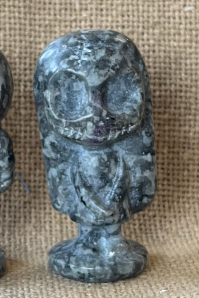 Gray and black stone in the shape of Sally on a tan textured background.