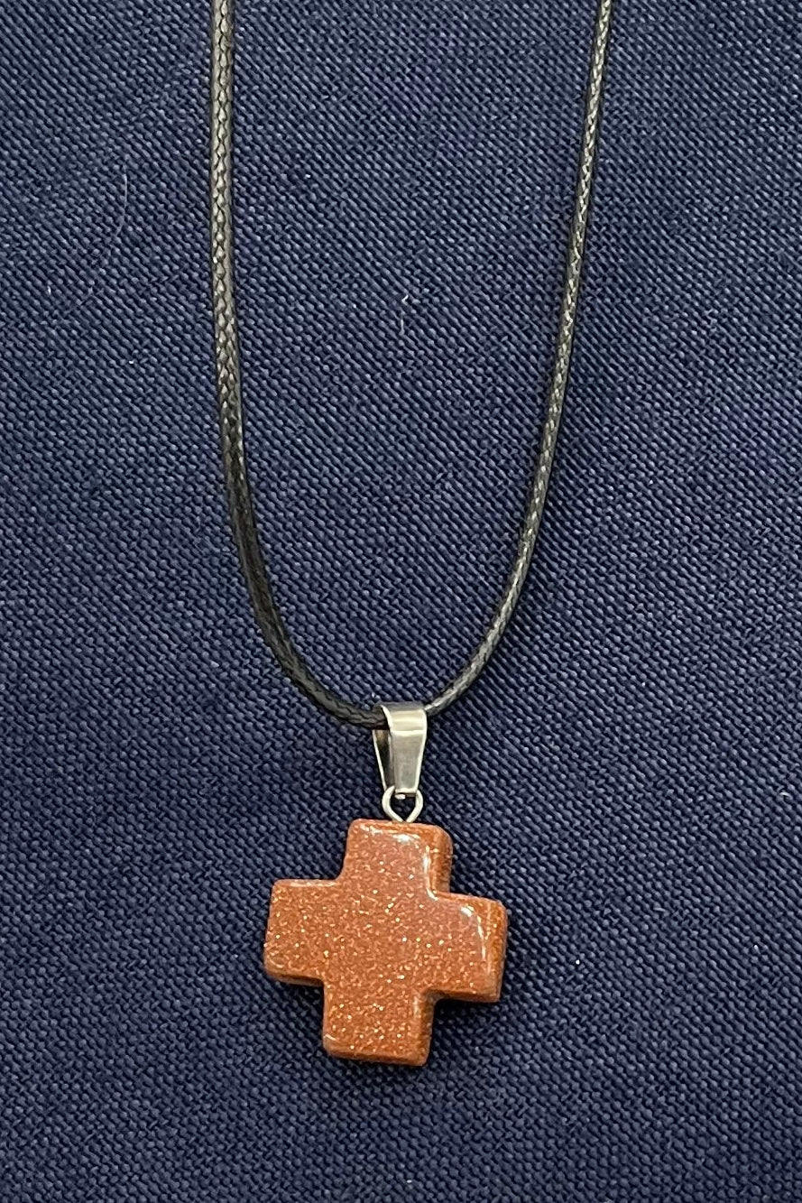 Orange-red sparkling medical cross pendant necklace on a blue fabric background 