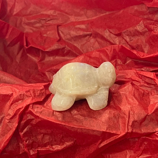 A small cream moonstone turtle figurine placed in the center of crumpled red tissue paper.